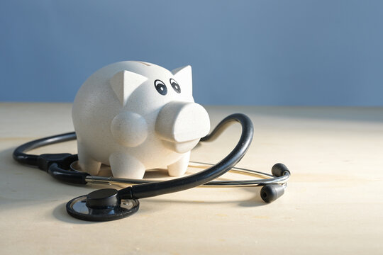 Piggy bank and a medical stethoscope on light colored wood against a blue background, concept for austerity measures in the healthcare sector, copy space