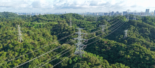 Aerial view of high voltage electricity tower on green mountain with modern city in the distance © lzf