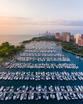 Aerial view of Belmont Harbor marina filled with numerous sailboats and motorboats, with the Chicago skyline in the background under a soft sunset sky, Chicago, Illinois, United States.