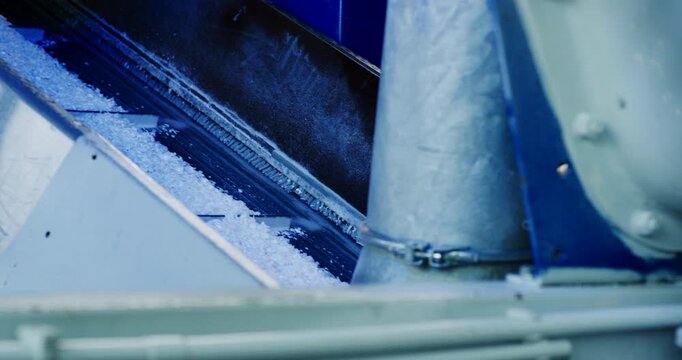 Industrial machinery processing raw white plastic material through a metal tube and chute system
