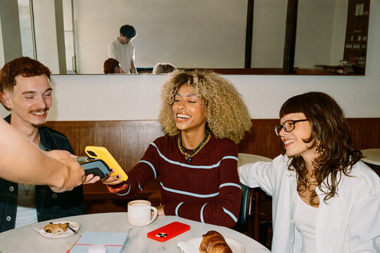 Young friends in a cozy coffee shop making a contactless payment