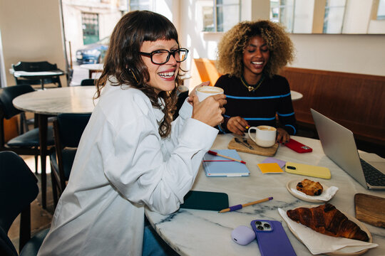 Two friends laughing over coffee and working in a caf&eacute;