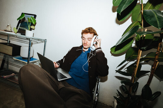 Young man multitasking with laptop and headphones in home office