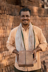 Obraz premium Indian brick maker standing proudly in front of stacked clay bricks