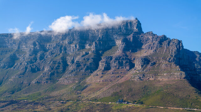 Aerial view of Table Mountain featuring clouds on its flat summit, rugged rock faces, and green slopes Cape Town, Western Cape, South Africa.