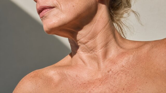 Close-up of mature woman neck and shoulder skin texture with natural wrinkles and light shadows