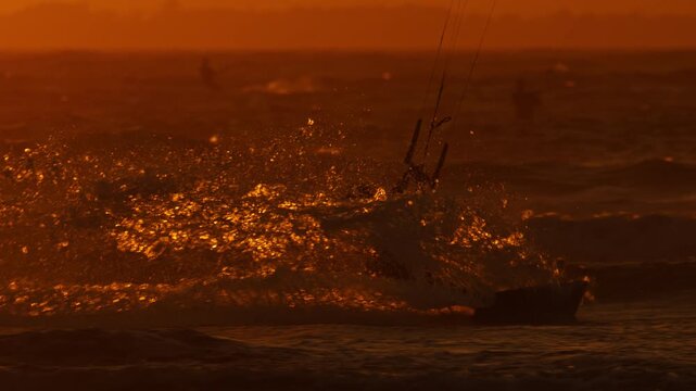 Sunset kiteboarding session as guy carves through water, telephoto slomo