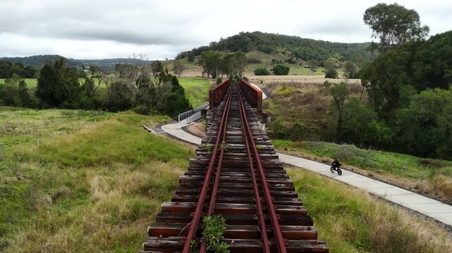 A female riding an e-bike travels along a bike path that follows a disused railway corridor with heritage-listed bridges and expansive vistas.