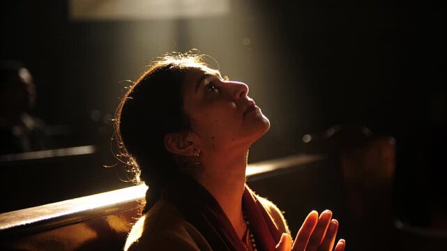 Gazing worshipper clasping hands on pew reacting to falling shaft of light with maroon scarf
