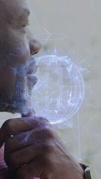 Vertical video: Senior man holding gizmo at chin, moving lips and making holo grow into tech globe