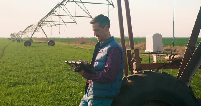 Farmer walking in wheat field setup irrigation system on tablet.