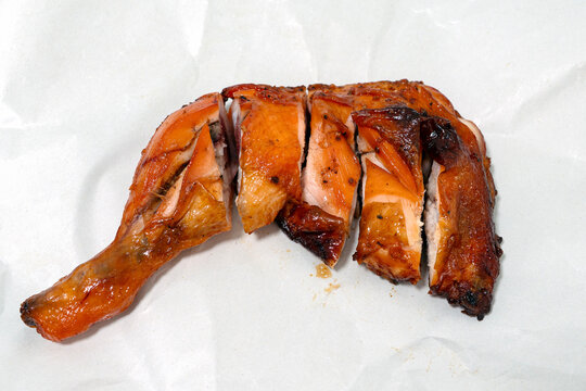Thai grilled chicken background with crispy skin and cut pieces on white paper.