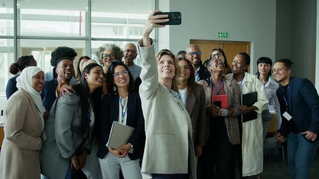 A cheerful group of colleagues and attendees happily pose for a group selfie at a conference or professional event. Their genuine smiles and laughter reflect a moment of positive connection.