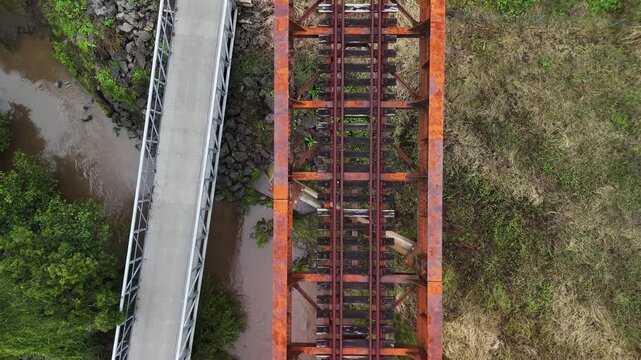 Northern Rivers rail trail bike path winding below an old rusty rail bridge spanning over a natural flowing creek and pedestrian bridge. Drone view