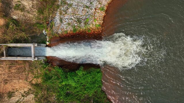 Aerial drone view of water flowing through a concrete irrigation channel into a reservoir, highlighting efficient water management, agricultural sustainability, and controlled distribution systems.
