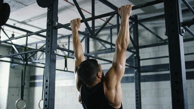 Starting dead-hang, man in black tank top performing pull-ups on pull-up bar at gym for strength