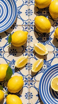 Top-down flat lay of fresh yellow lemons and striped ceramic plates on beautiful blue and white decorative tiles. Hard summer sunlight with sharp shadows. Mediterranean aesthetic and food concept