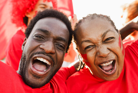 African red sport fans screaming while supporting their team - Football supporters having fun at world soccer competition event - Main focus on faces