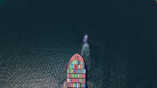 High aerial top-down view of a massive cargo container ship sailing across the deep blue ocean, carrying colorful intermodal containers for international shipping and global trade