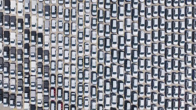 Hundreds of new cars parked in a vast lot at an automotive factory, creating a geometric pattern of vehicles waiting for distribution, symbolizing mass production and global trade