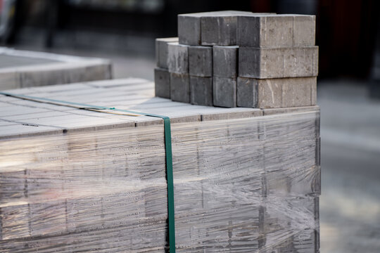 Industrial concrete brick pavers neatly packed with stretch wrap and green strapping for hardscaping and public infrastructure projects