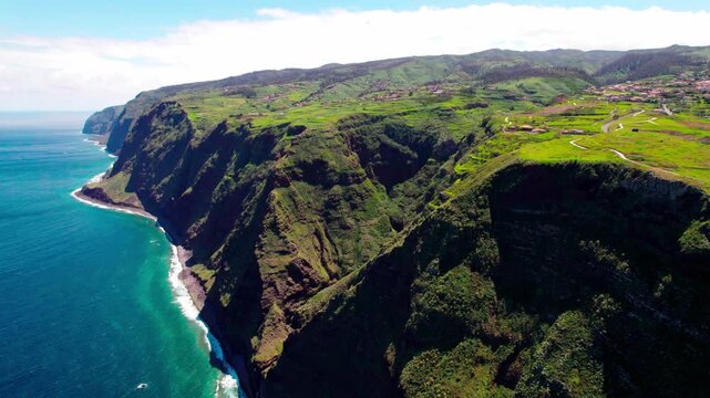 Drone aerial zoom in capturing towering volcanic cliffs, green plateaus and the deep blue Atlantic Ocean along Madeira's rugged coastline.