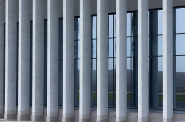 Naklejka premium Modern building facade with vertical white columns and dark glass windows. Repeating architectural lines create a clean contemporary exterior. Ideal