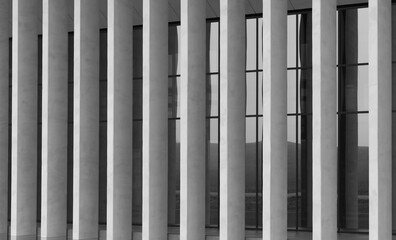Obraz premium Modern building facade with vertical white columns and dark glass windows. Repeating architectural lines create a clean monochrome exterior. Ideal for