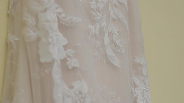 Closeup of white wedding dress with delicate floral lace embroidery and beaded detail