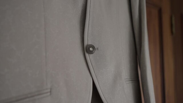 Closeup of beige suit jacket button and front pocket on tailored fabric