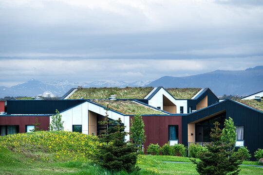 View of modern residential buildings with green turf roofs and triangular gables under a cloudy sky with distant mountains in Reykjavik, Reykjavikurborg, Iceland.