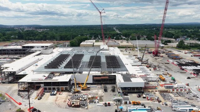 Data center campus in Lancaster shows rooftop cooling arrays, red and yellow cranes, steel-framed expansion, and stacked materials on sprawling site. Pennsylvania, USA. Aerial drone backwards shot