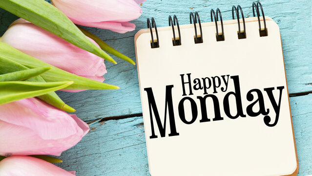 Happy Monday words in a notebook next to tulips on a blue table.