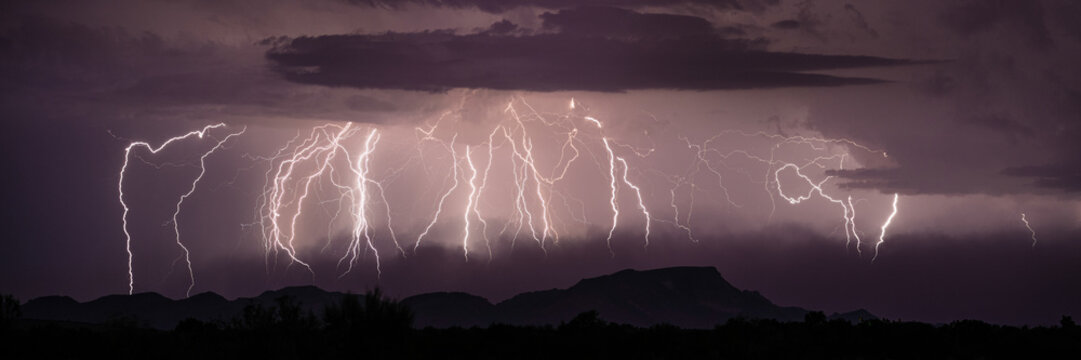 View of multiple lightning bolts striking over dark mountain silhouettes during a powerful thunderstorm in Kanab, Utah, United States.