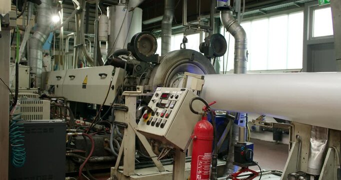 Industrial machinery extruding a thick white pipe in a manufacturing facility