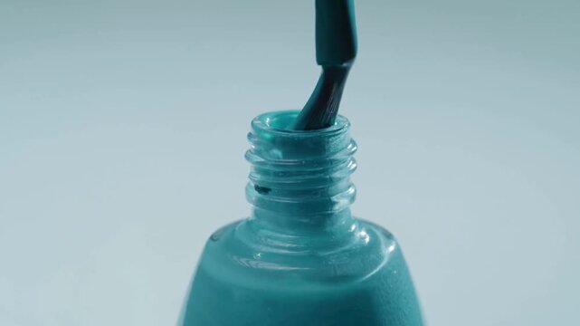 Macro of blue nail polish brush dipping into bottle neck closeup, liquid varnish texture dripping in slow motion, professional salon manicure cosmetics product concept 4K video