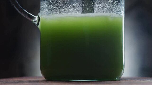 4K Video macro close up of fresh green juice or matcha tea being mixed with a spoon in a glass pitcher jar, creating swirling movement, foam, and bubbles for healthy diet and lifestyle.
