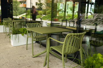Obraz premium Stylish contemporary green metal dining table with chairs stands on an outdoor patio of a restaurant or residential courtyard, surrounded by modern landscaping and white planters.