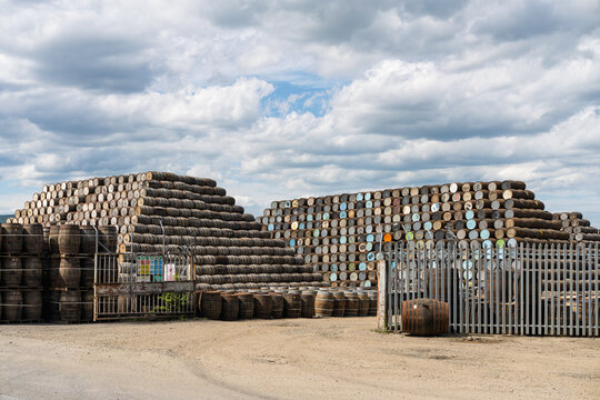 Weathered wooden barrels for Scotch whisky maturation neatly stacked at a Cooperage facility during the day