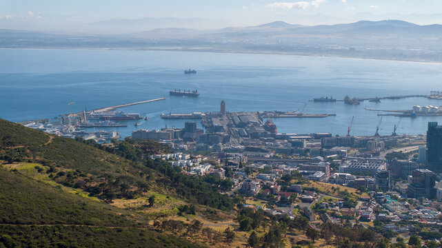 Aerial view of the bustling Cape Town harbor and VA Waterfront, featuring cargo ships, urban architecture, and coastal mountain slopes in Cape Town, Western Cape, South Africa.
