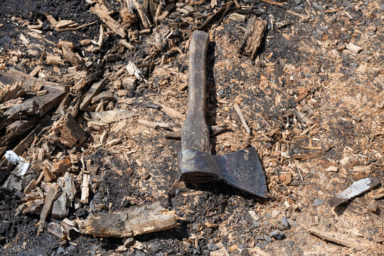 a weathered, old iron axe with a wooden handle lying on a ground covered in wood chips and dark debris