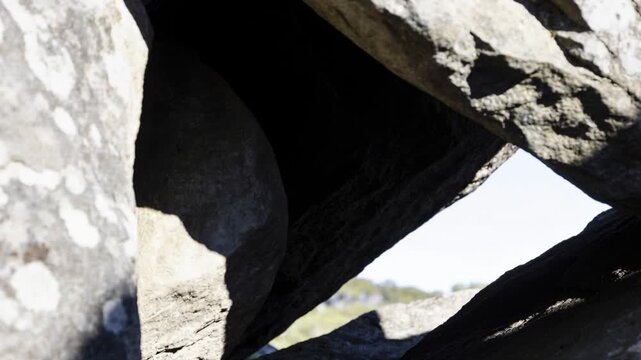 Moving camera revealing triangular crevice in stacked boulders at outcrop, showing lichen and sky