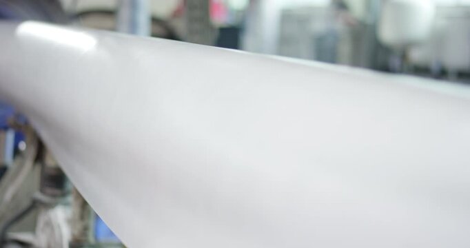 A wide roll of white paper rotating on a spindle in a manufacturing plant