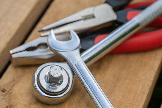 a collection of essential metal hand tools, including a chrome socket wrench, a spanner, and red-handled pliers, resting on rustic wooden pallet boards.