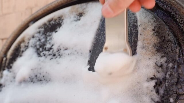 Hand scraping soot from fireplace with metal scraper and foam close-up