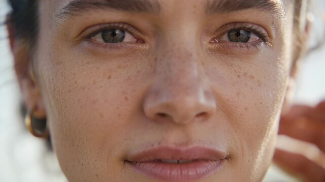 Shifting gaze woman with freckles and gold hoops posing outdoors as camera centering, tucking hair