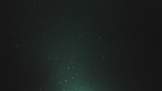 Floating dust particles in dark water with light source from below.