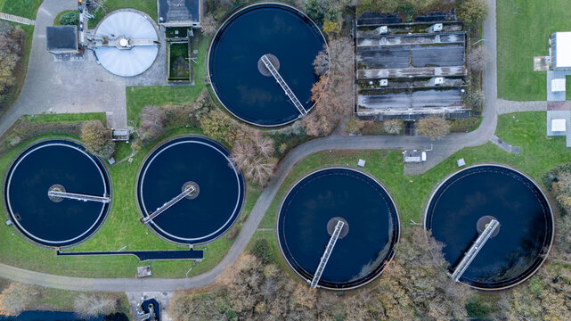 Top down aerial view of a wastewater treatment plant with circular clarifier tanks, water basins, service roads and technical infrastructure. Industrial water management facility seen from above.