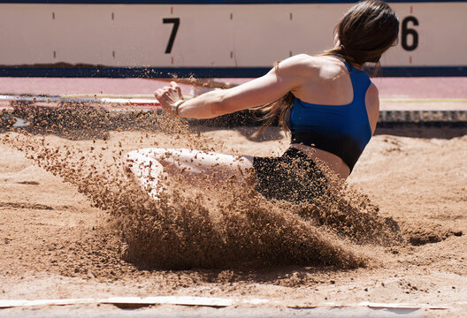 Female athlete long jump landing sand spray, landing in long jump in track and field