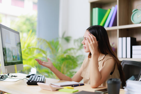 Young asian business woman feeling stressed, confused, and frustrated in the office, experiencing a computer problem or encountering a workload issue at her desk